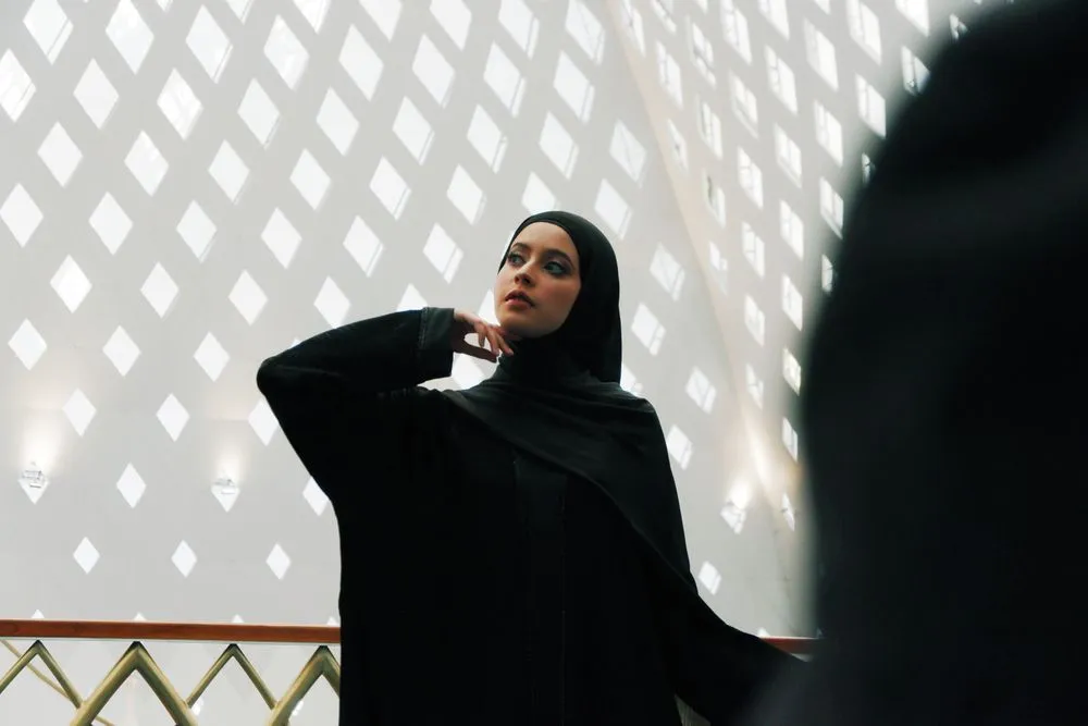 Woman in a black abaya standing before a white latticed wall